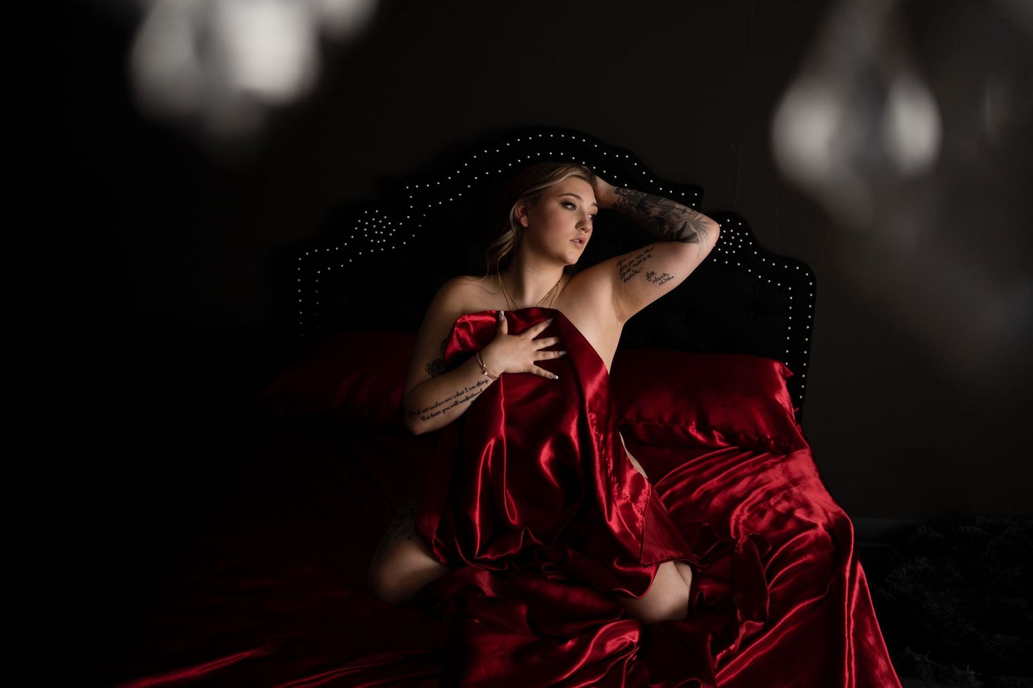 Dramatic boudoir portrait with flowing red fabric in moody lighting.