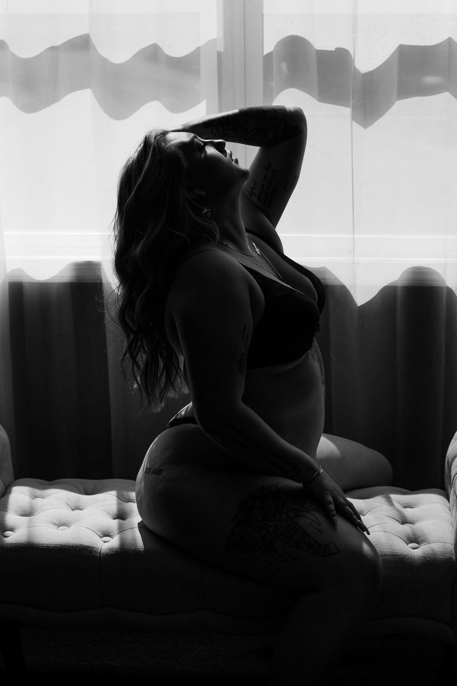 Silhouette figure poses by window in artistic black and white boudoir photography.