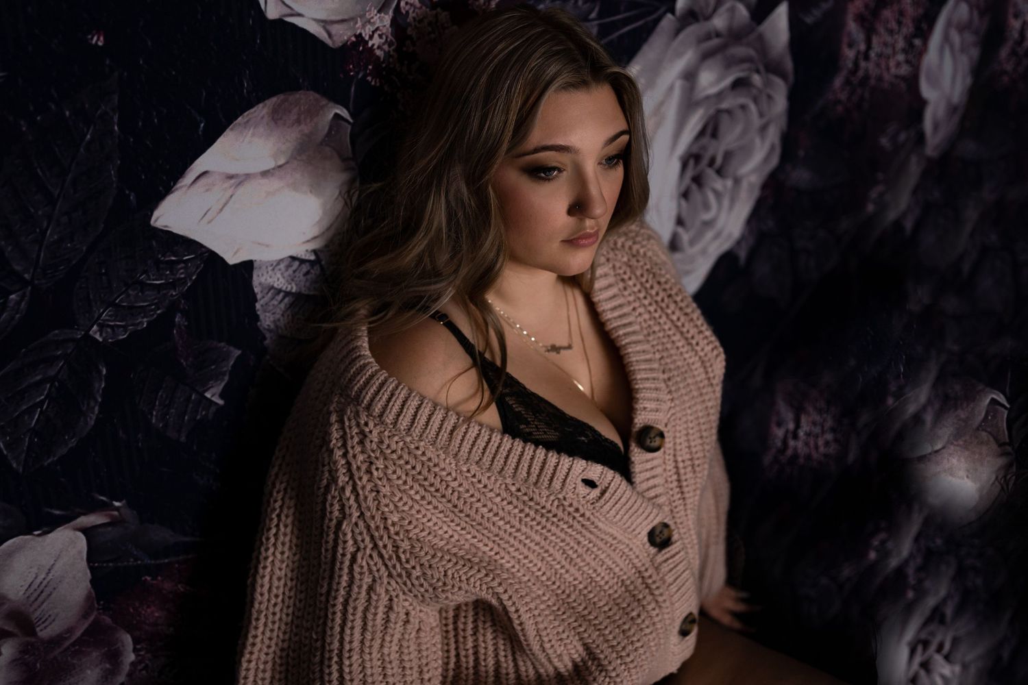 Cozy winter boudoir portrait featuring a knit sweater against dark floral backdrop.