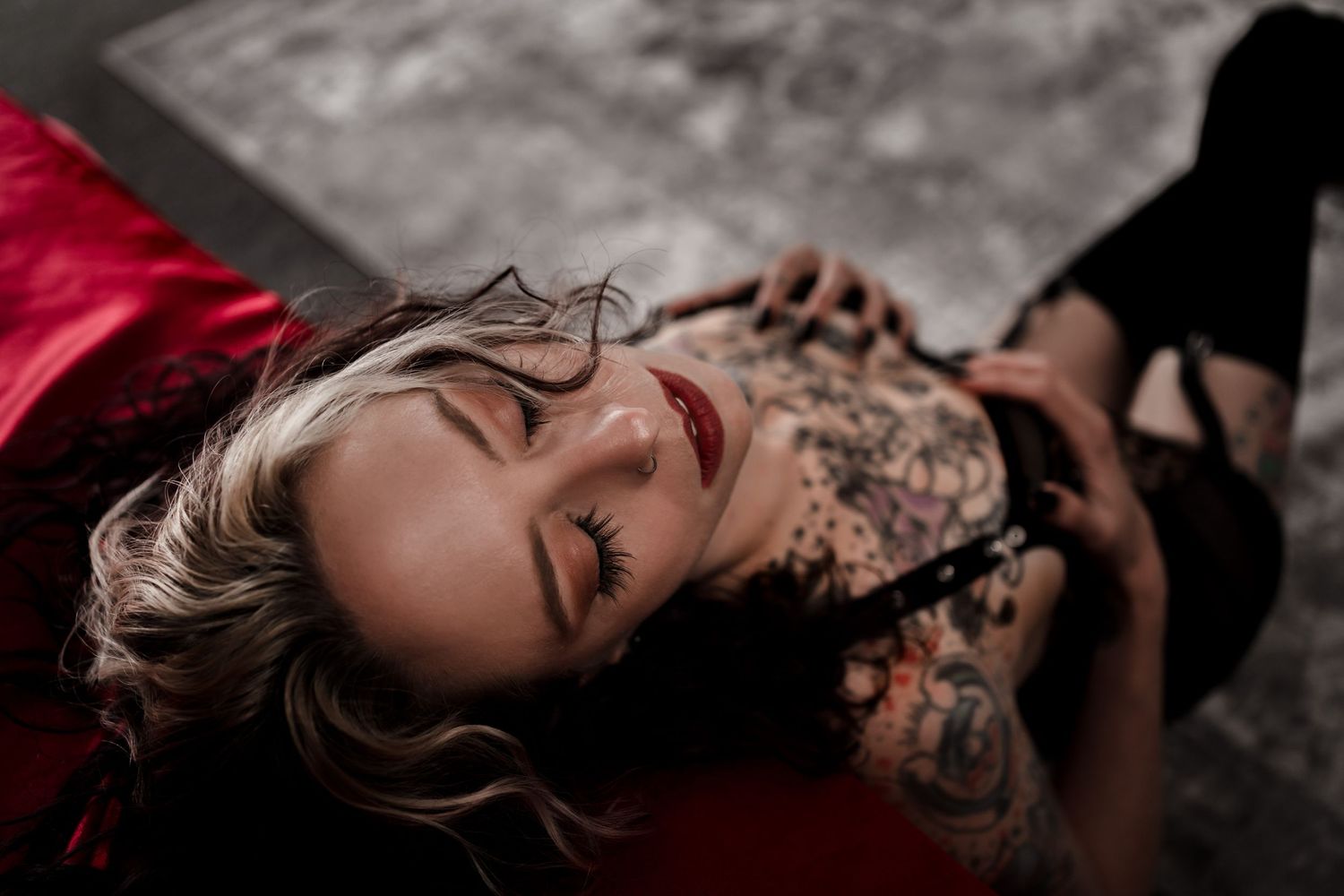 A moody boudoir portrait of someone lying on red fabric wearing lace.