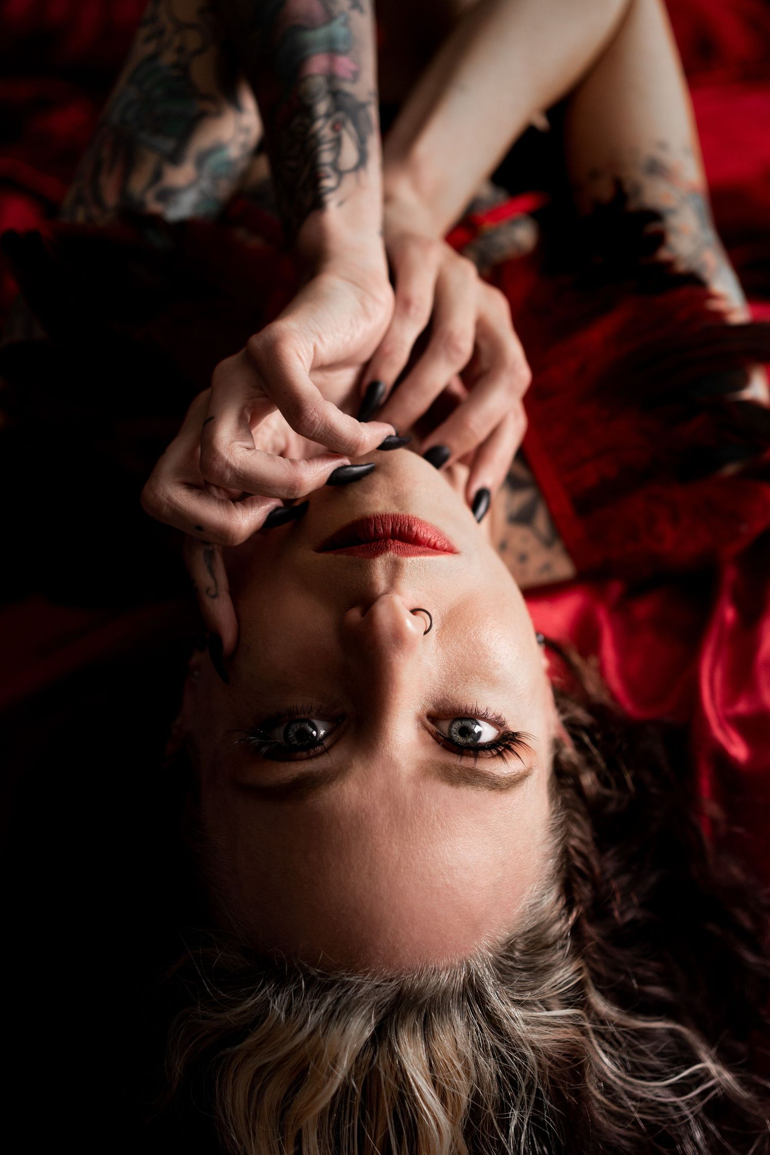 Intimate boudoir portrait with dramatic lighting and red lipstick against crimson fabric.