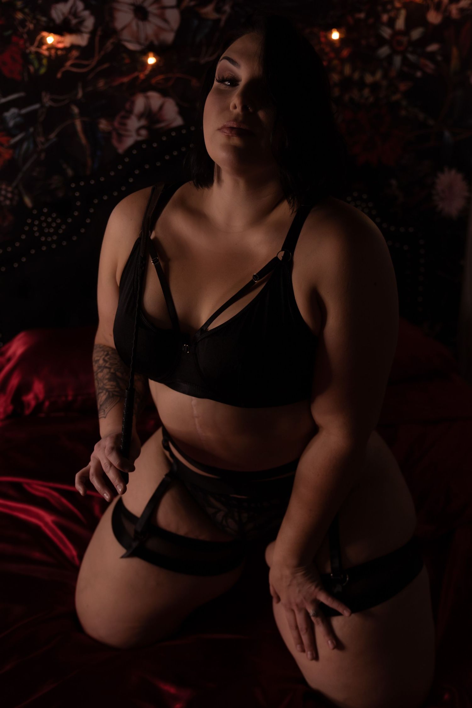 Artistic boudoir photoshoot in dark moody lighting with black lingerie and red accents.