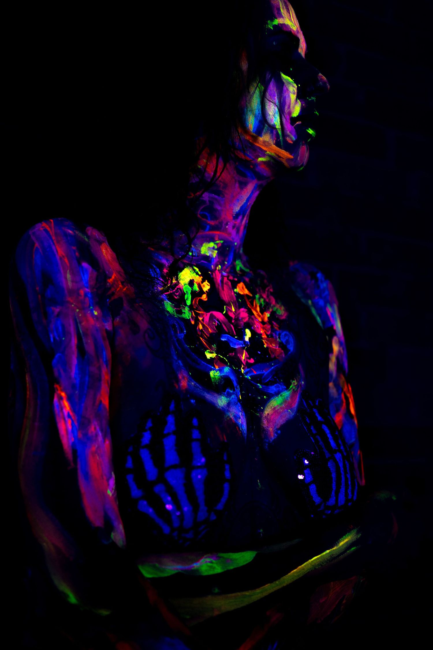 Neon body paint creates psychedelic patterns and shapes in dramatic black light photography.