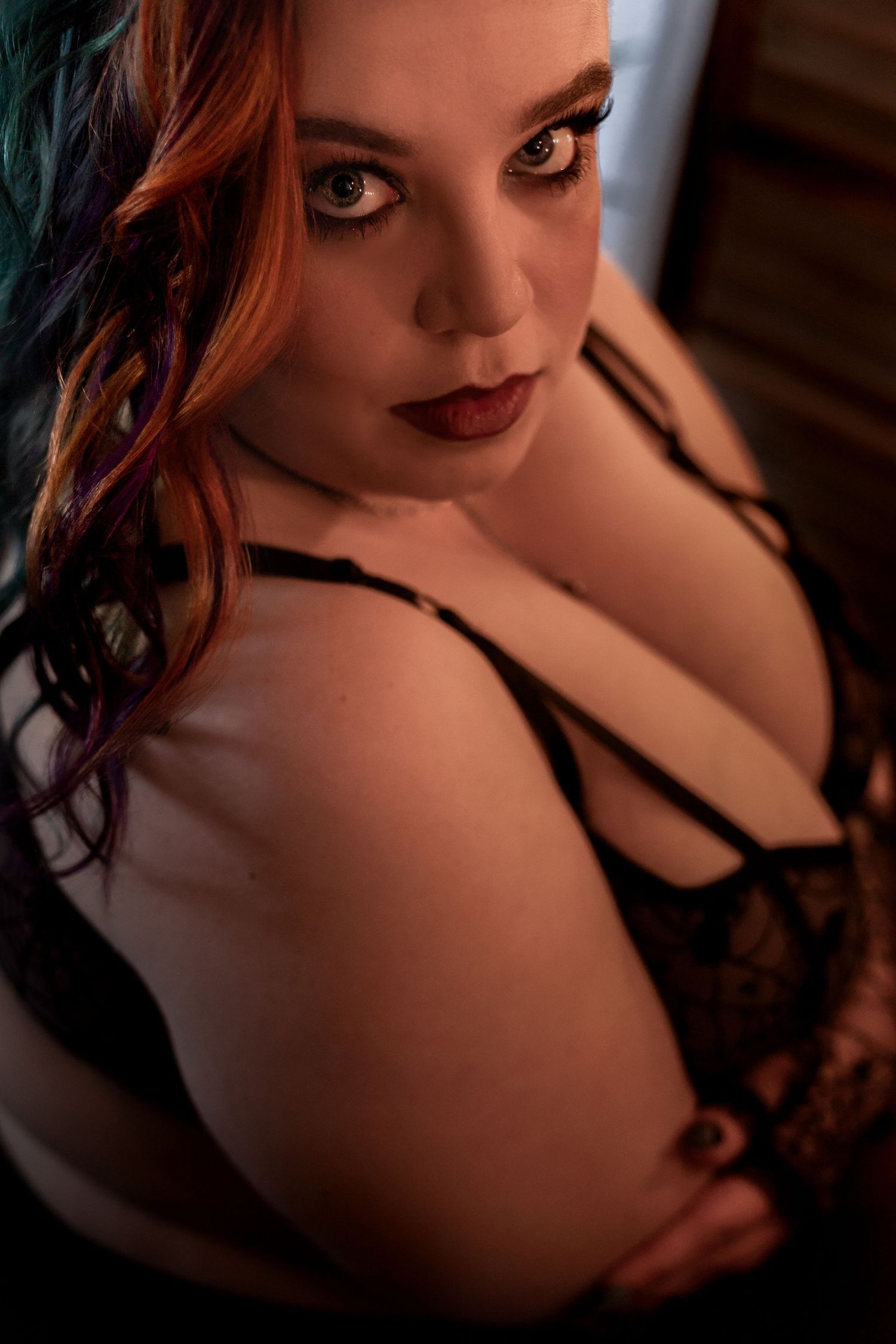 Moody boudoir portrait featuring dark lace lingerie and dramatic lighting.