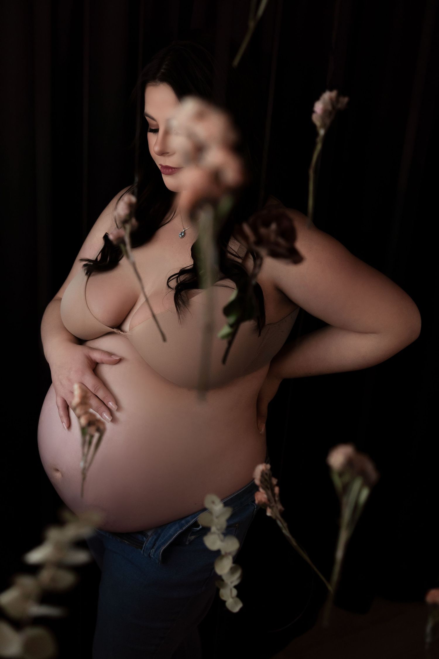 Artistic maternity portrait with delicate white flowers against dark background.