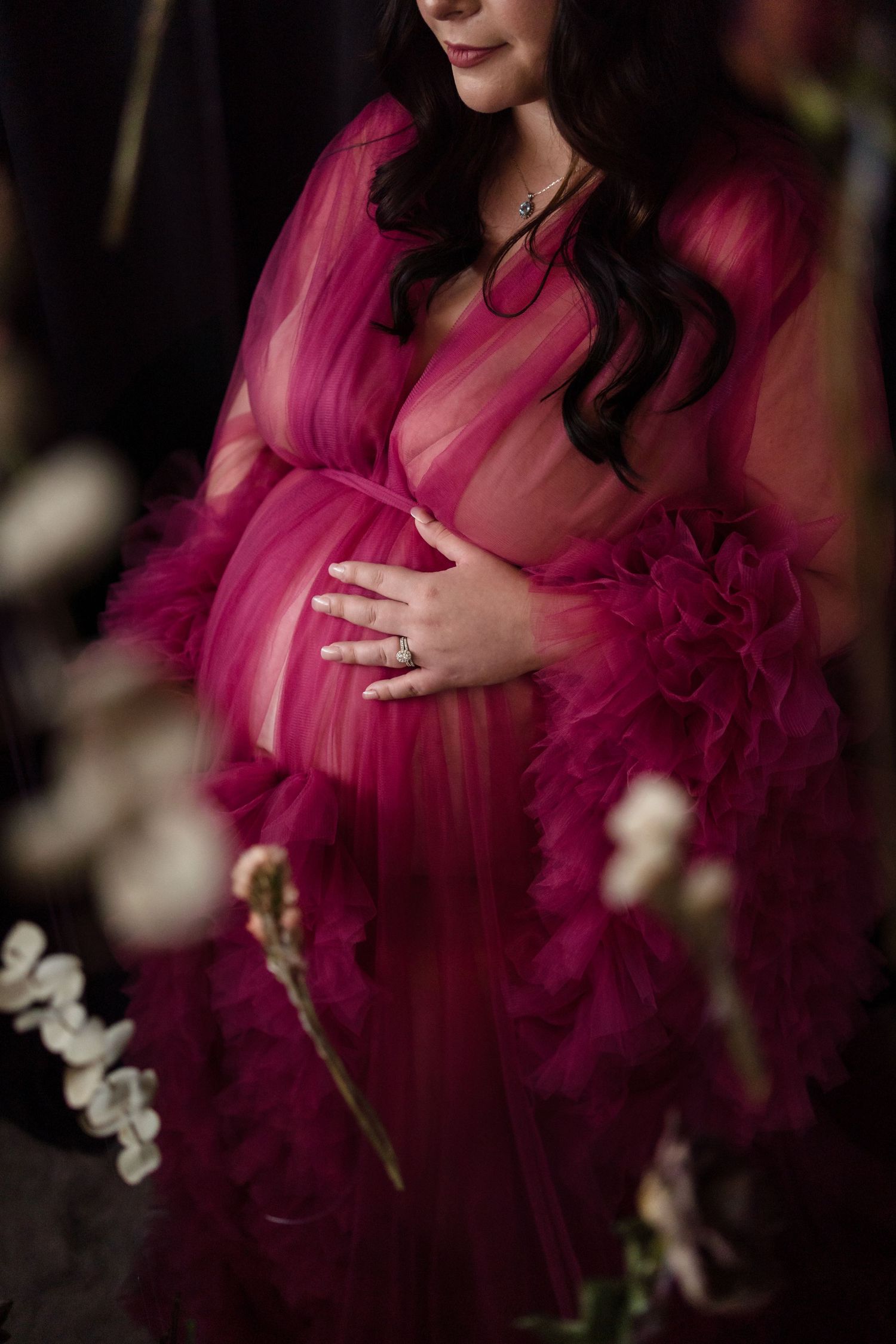 Maternity portrait in flowing magenta tulle gown with white floral accents.