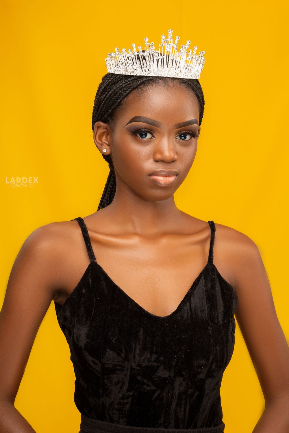 Elegant portrait featuring crystal crown and black velvet top against vibrant yellow background.