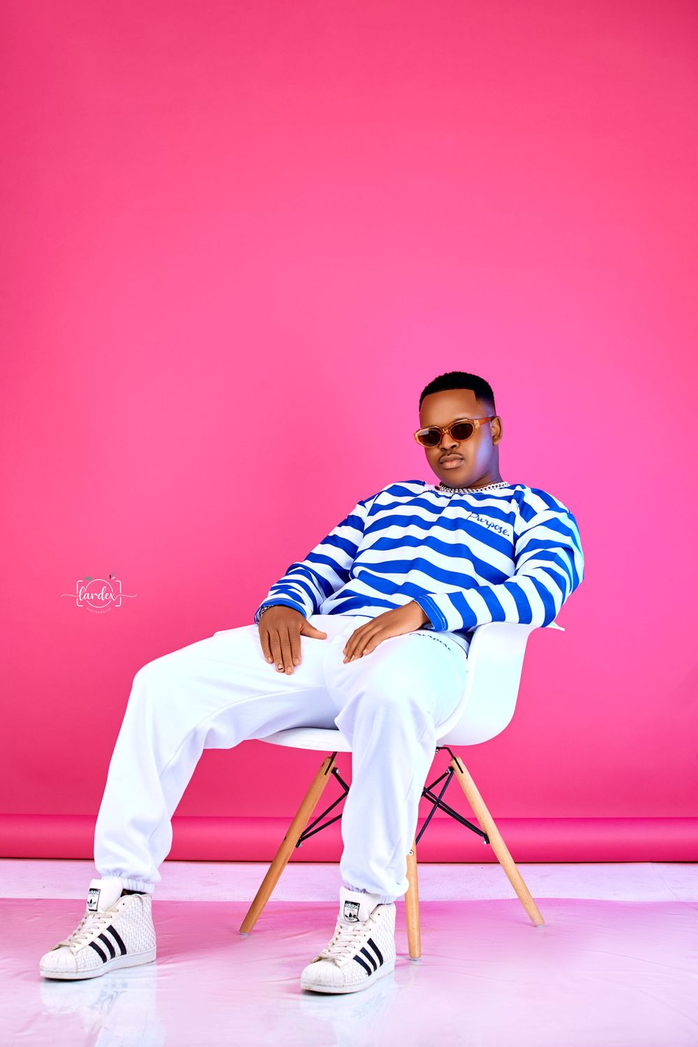 Person in striped blue and white sweater relaxes in modern white chair against pink backdrop.