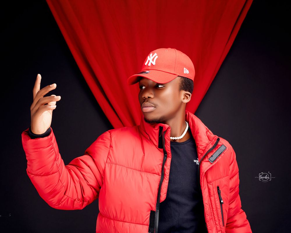 Person in red puffer jacket and NY cap poses expressively against red backdrop.