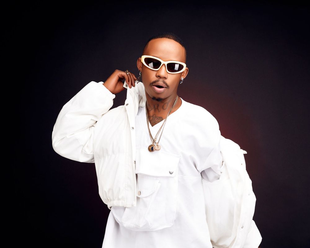 Person in white outfit and sunglasses poses confidently against dark background.