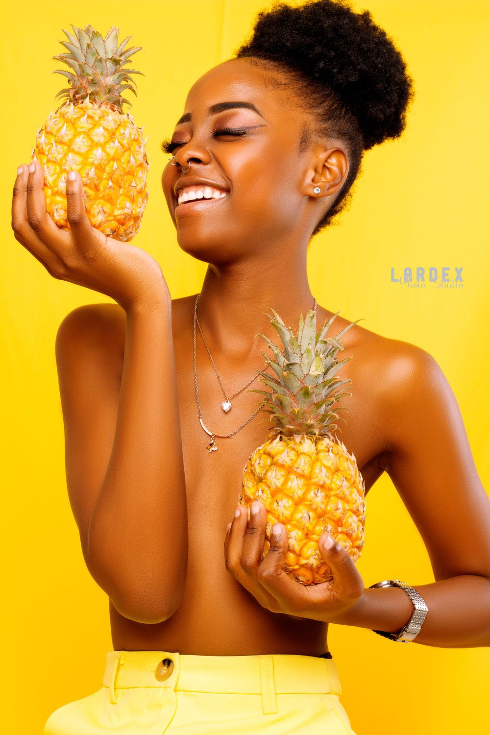 Cheerful summer portrait with pineapples against yellow background showing natural joy.