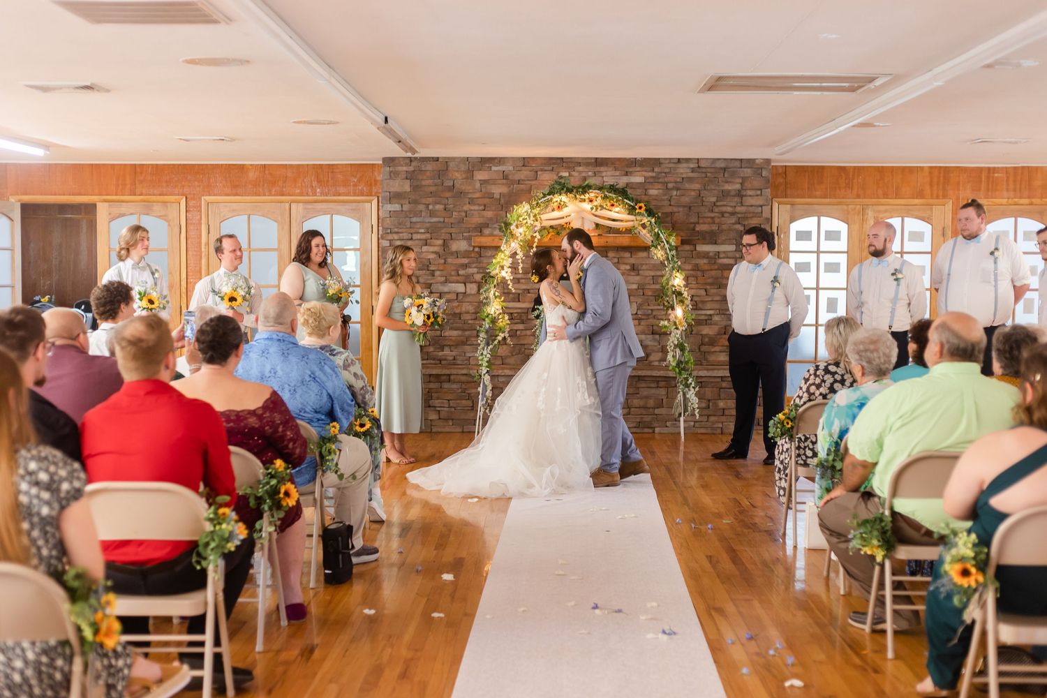 Wedding reception venue with exposed brick walls and hardwood floors filled with guests.