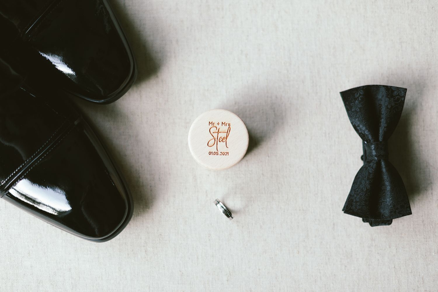 Black formal shoes with bow tie and wedding ring on light background.