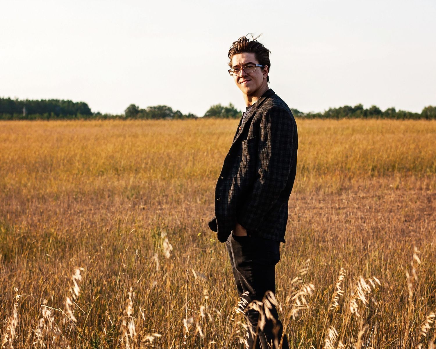 A person stands in a golden wheat field at sunset wearing a dark jacket.
