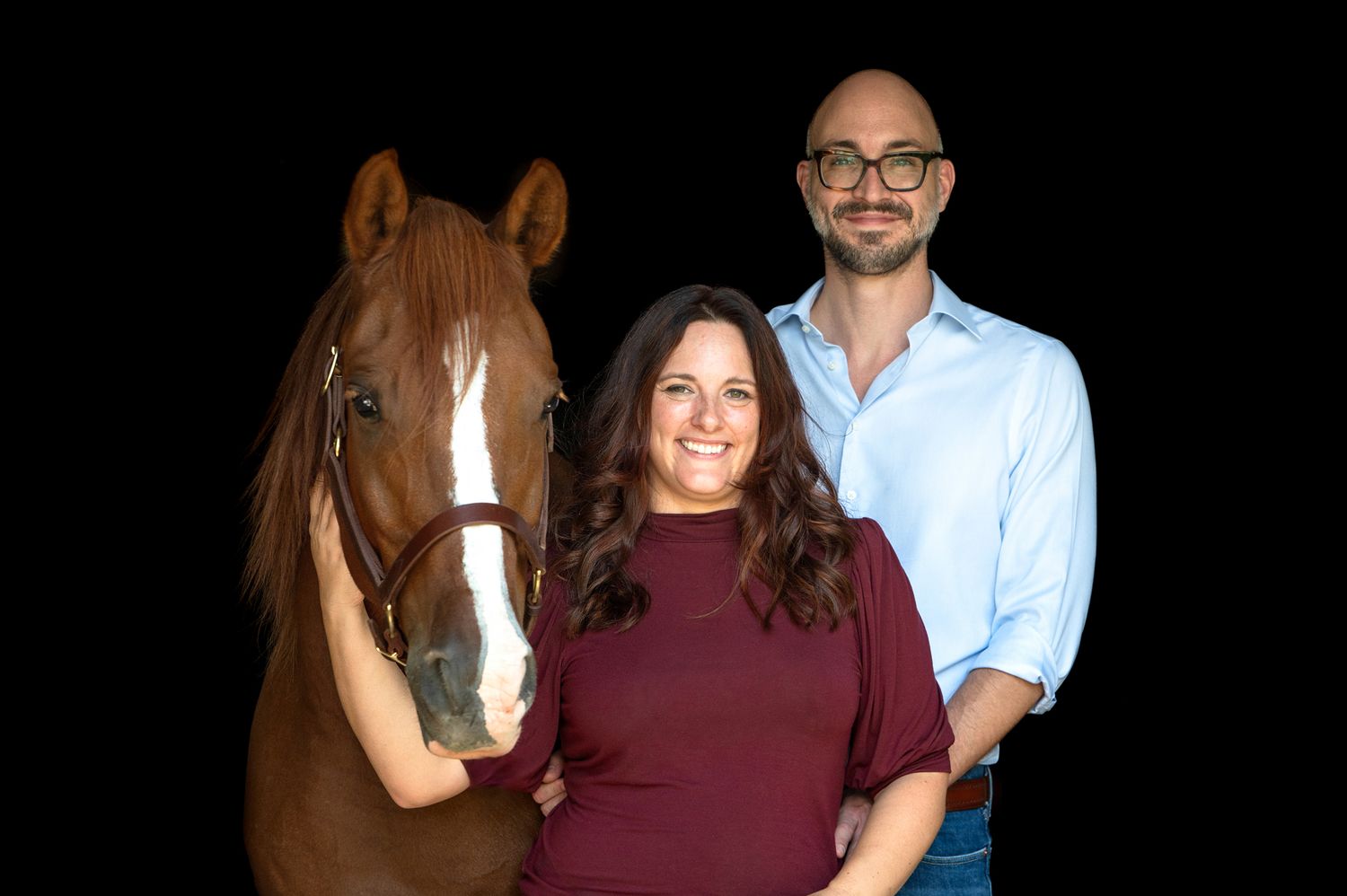 A beautiful chestnut horse with two people against a black background.