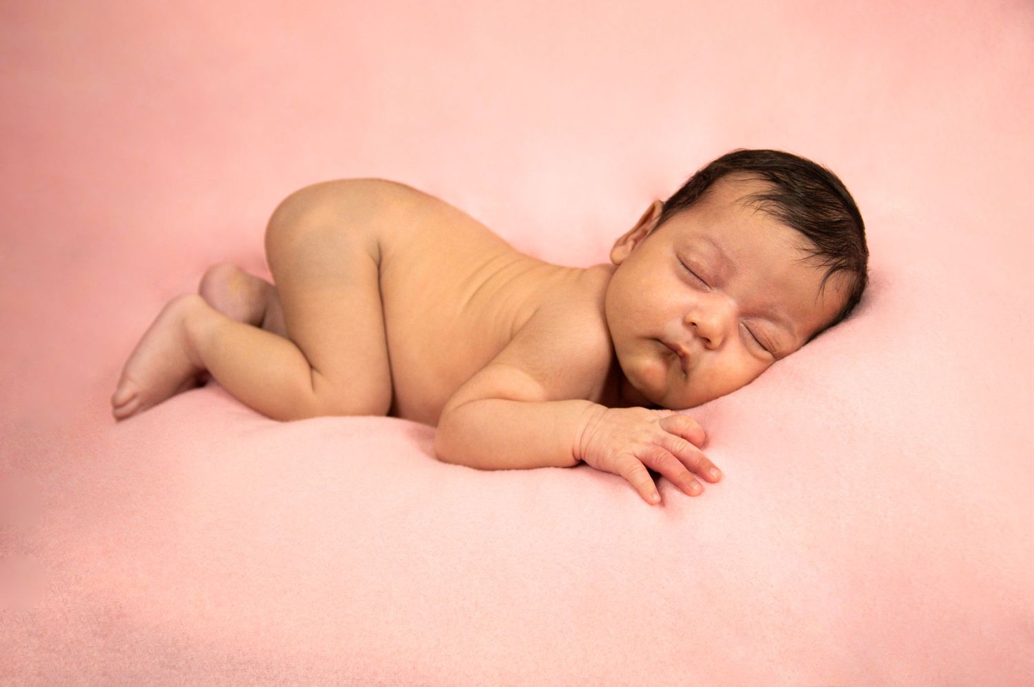 A peaceful sleeping newborn lying on a soft pink backdrop during a professional photo session.