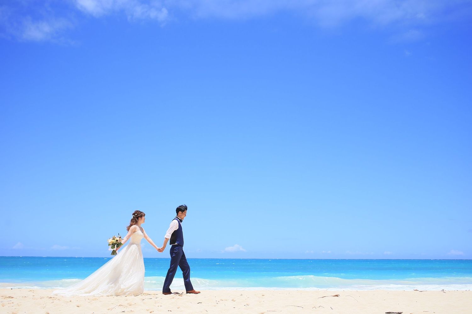 Wedding couple holding hands walking on tropical white sand beach with turquoise ocean.
ハワイビーチウェディングフォト
ハワイ挙式