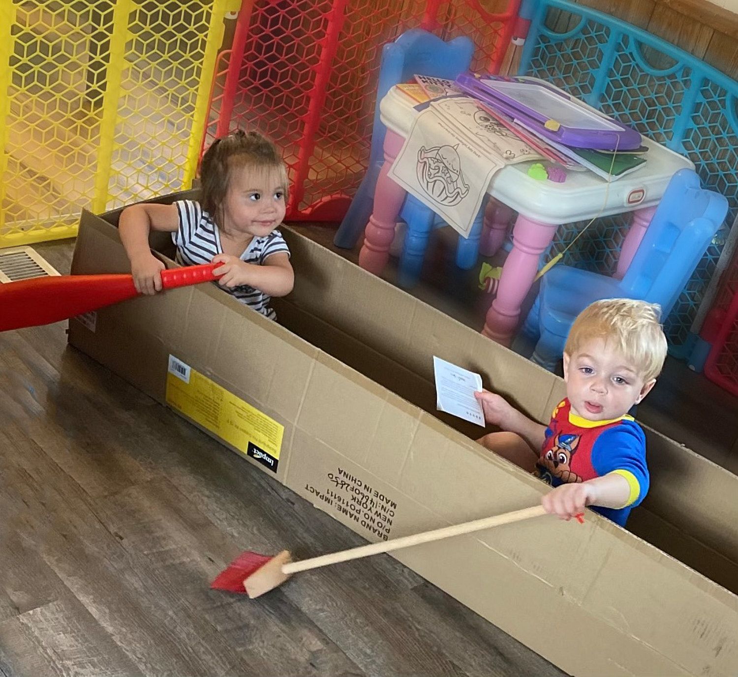 Toddler boy and girl playing row boat in a long shipping box