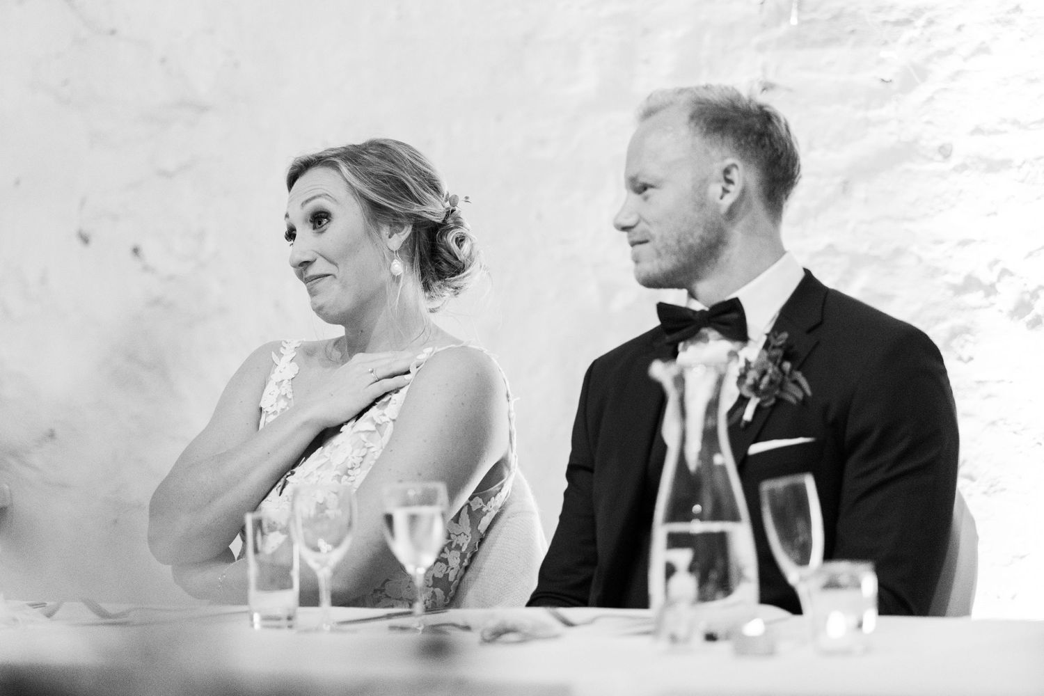 Black and white candid photo of a couple during wedding reception toasts.