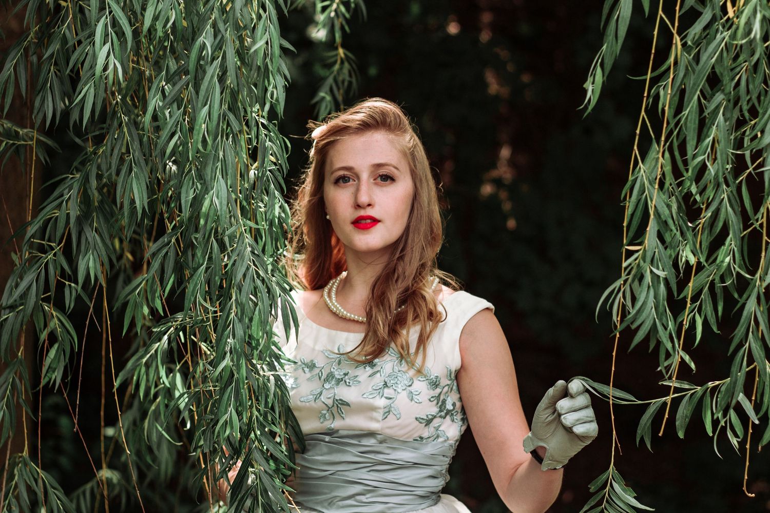 Women in elegant dresses pose beneath hanging willow tree branches.