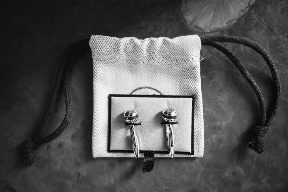 Silver cufflinks with decorative designs displayed in a white fabric pouch against a dark background.