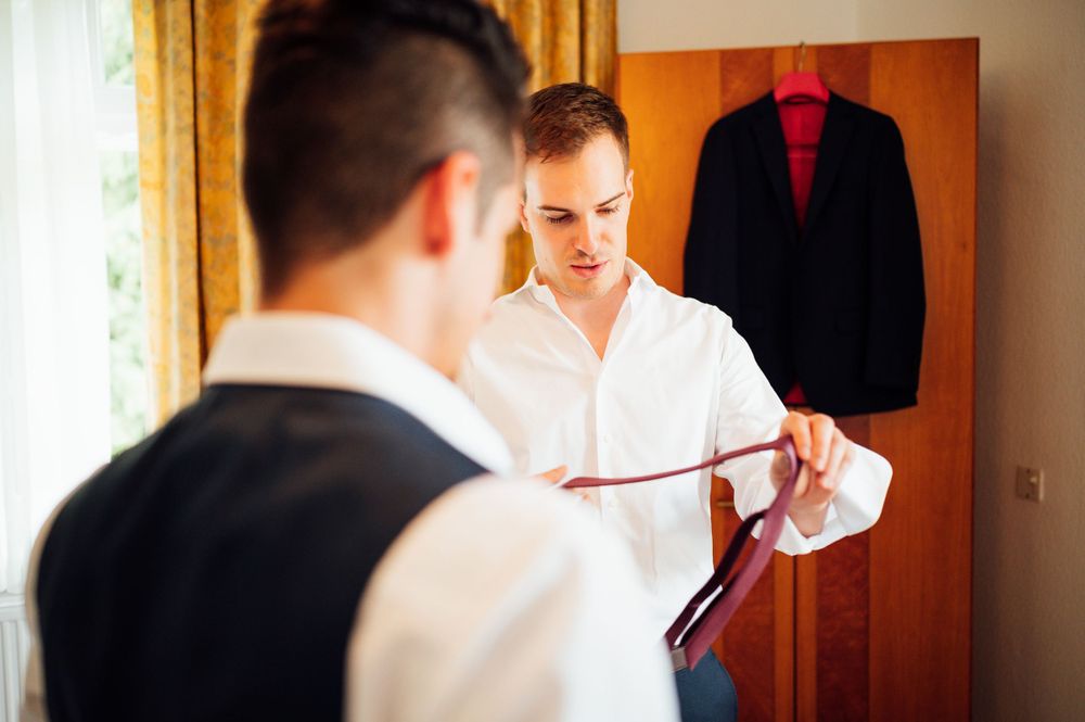Person selecting formal suit jacket with red tie hanging in hotel room wardrobe.