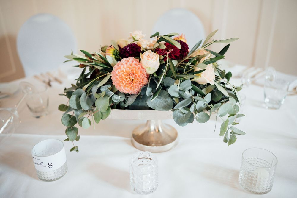A romantic wedding centerpiece with pink carnations, eucalyptus leaves and white candle holders on a white tablecloth.