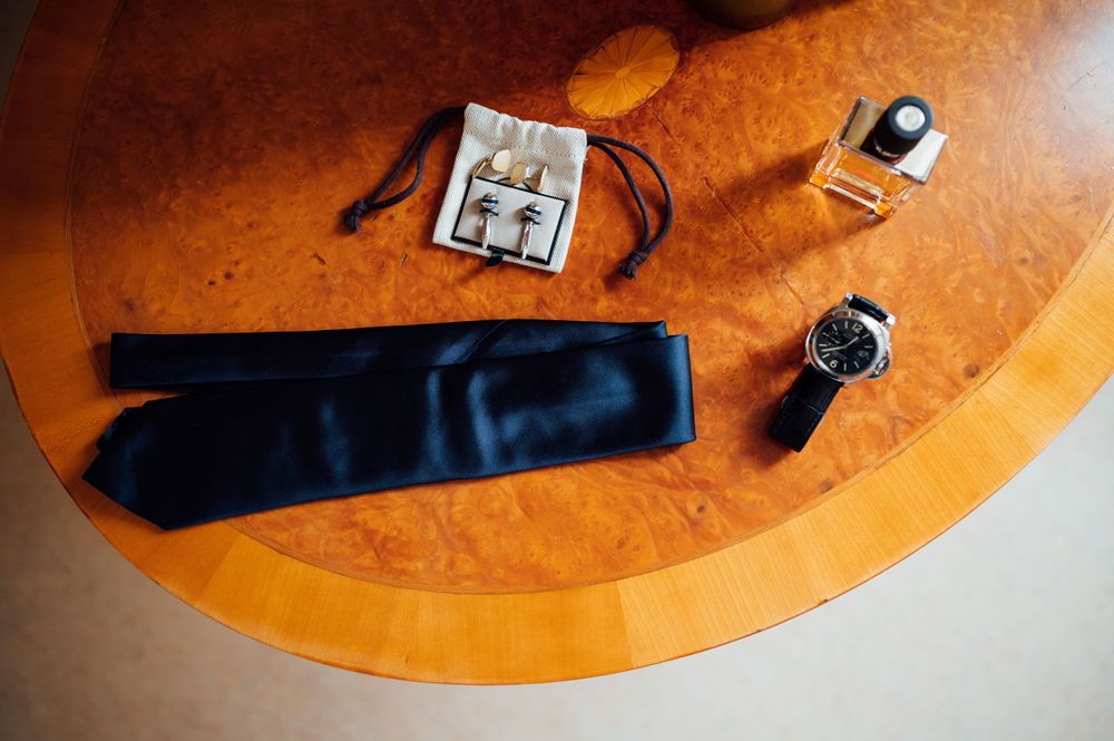 Wedding accessories including a blue tie, watch and cufflinks arranged on an orange surface.