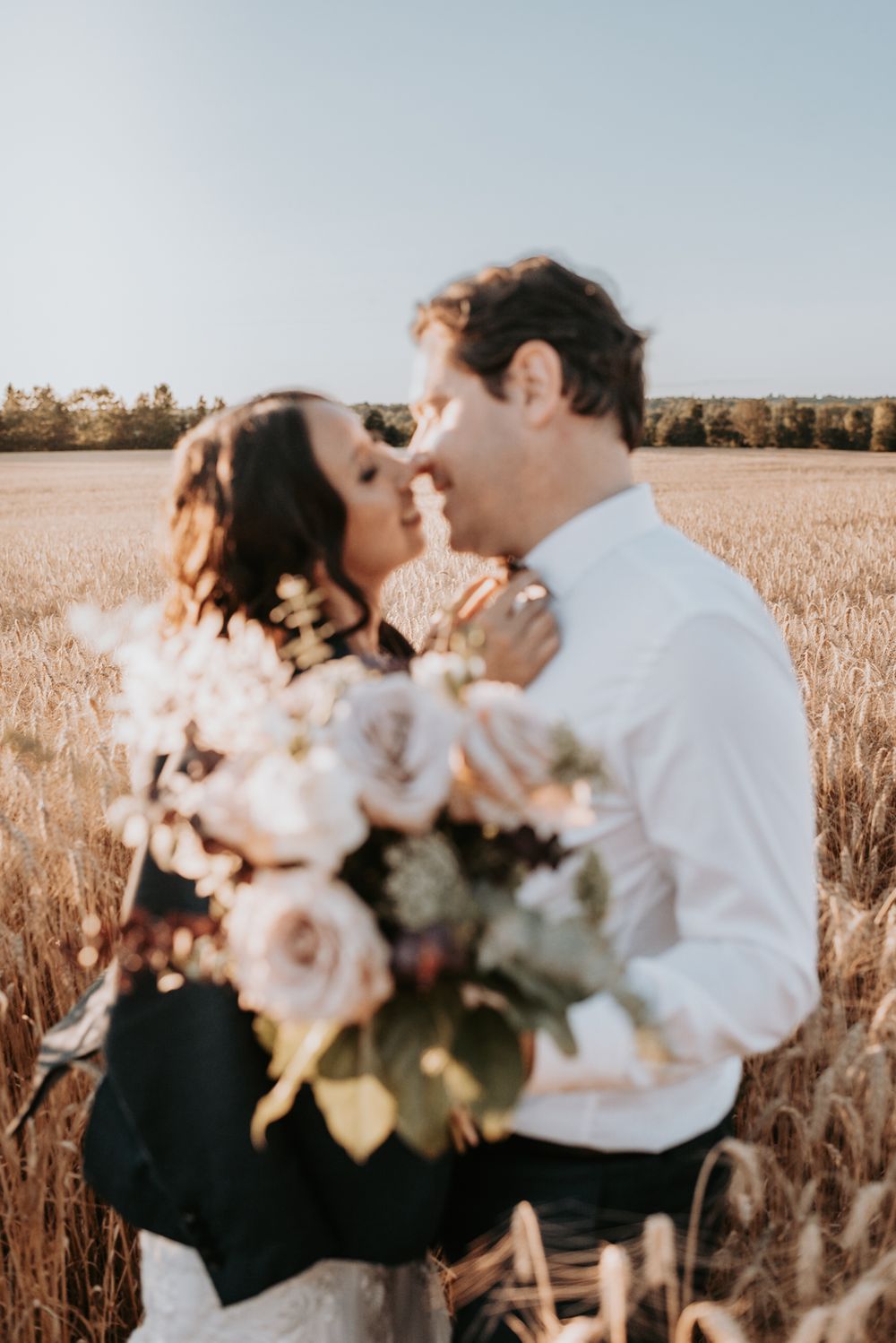 Couple embracing with bouquet of roses in sunlit wheat field.