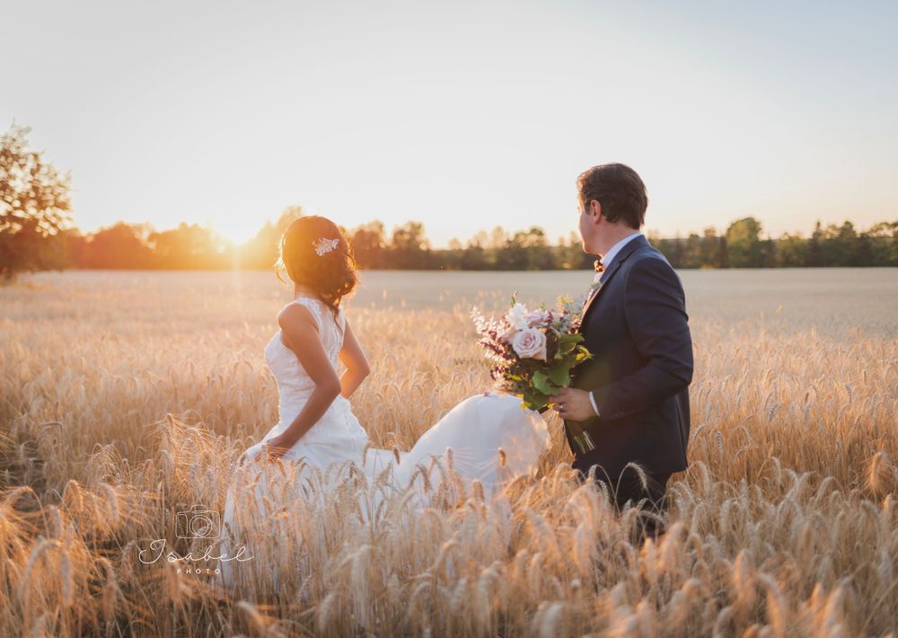 Romantic wedding couple embracing in golden wheat field at sunset with flowers.