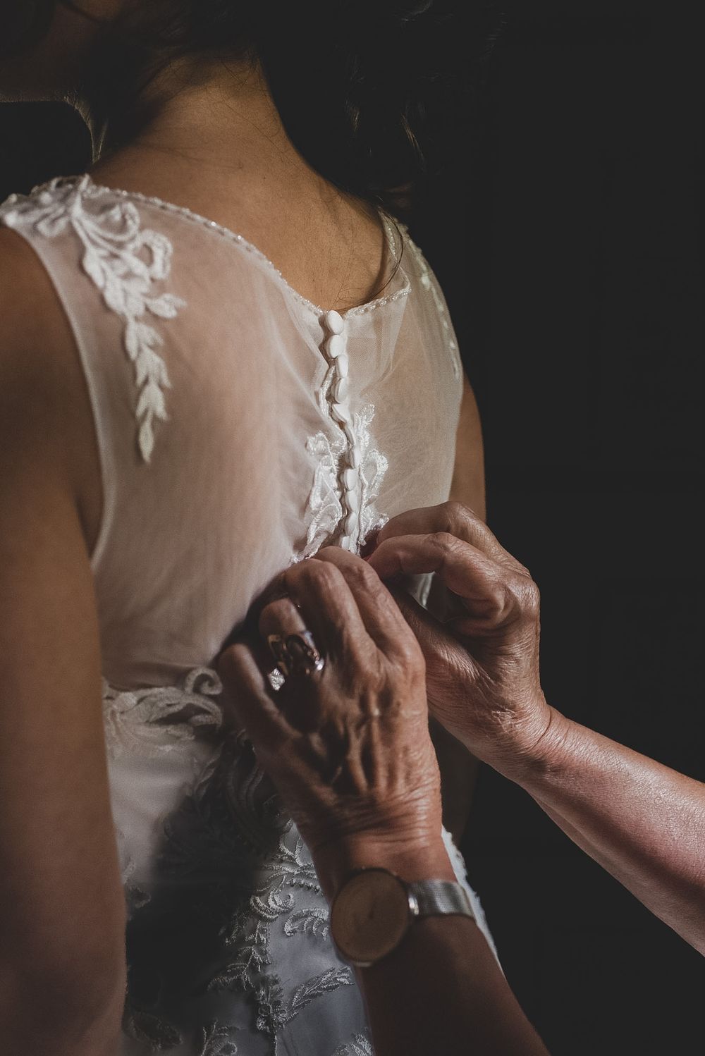 Closeup of hands buttoning or adjusting delicate white lace details on a wedding dress.