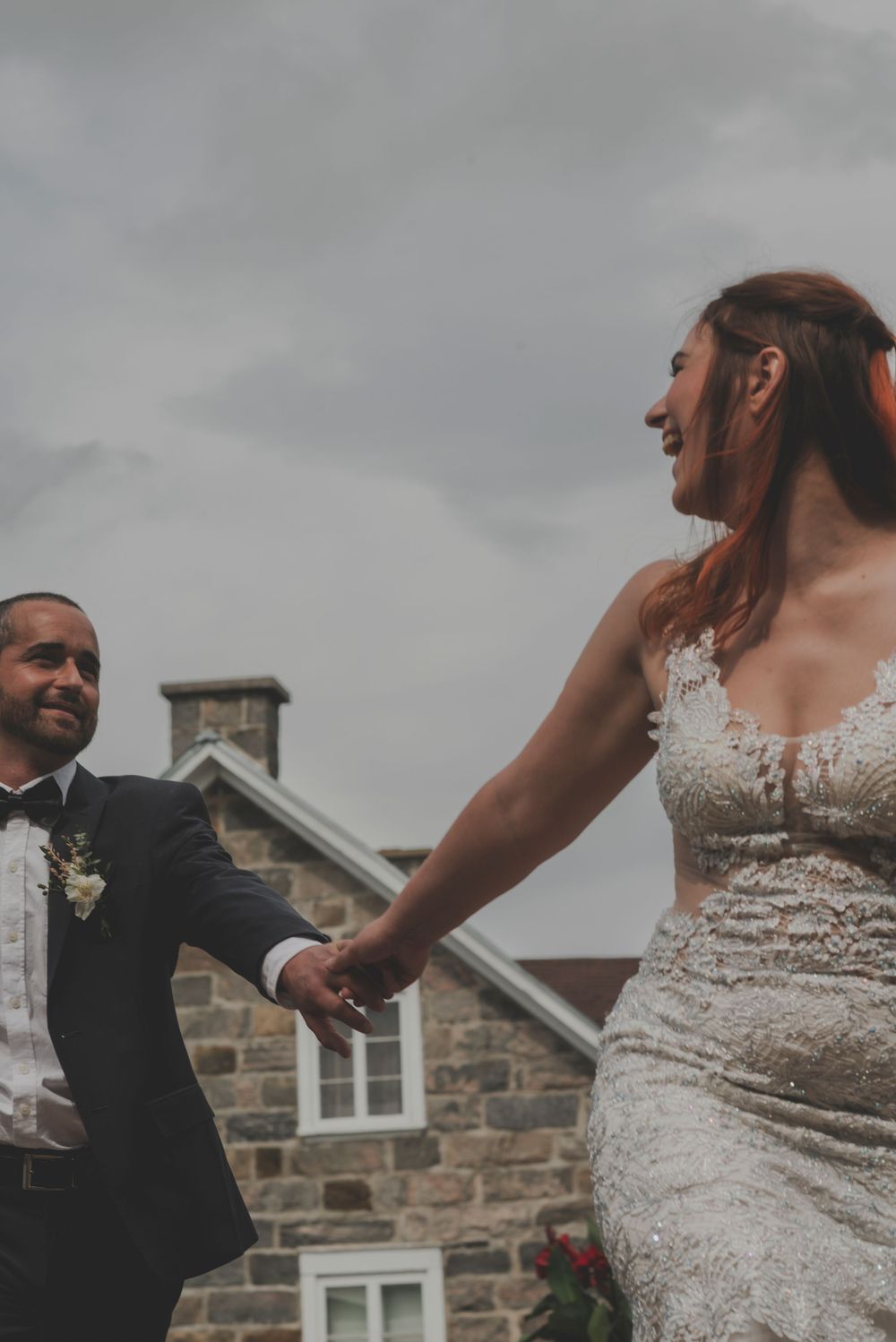 Wedding couple dancing playfully outside a rustic stone building.