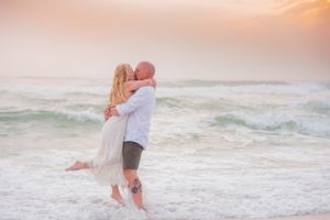 couple kissing on the beach as he holds her during fun engagement photoshoot in Panama City Beach Florida at sunset