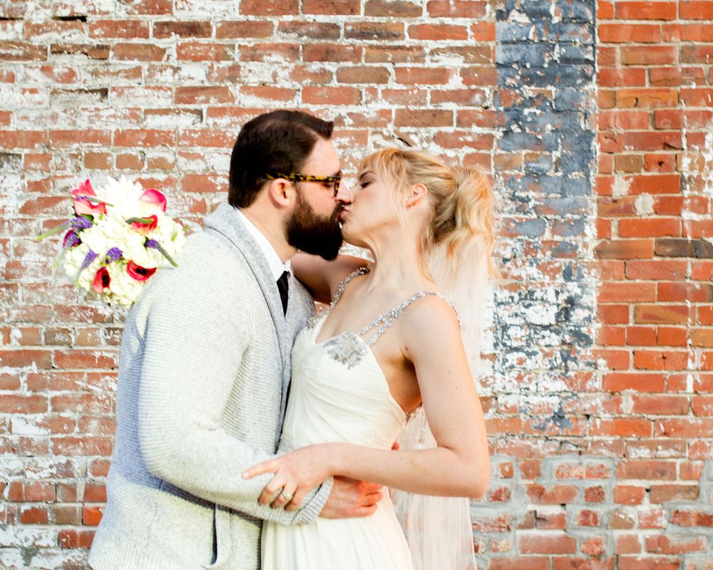 Wedding couple embraces in romantic sequence against vintage brick wall.