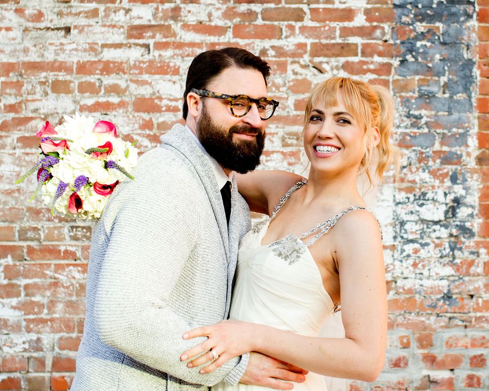 A romantic wedding photoshoot against a rustic brick wall backdrop with the couple sharing an intimate moment.