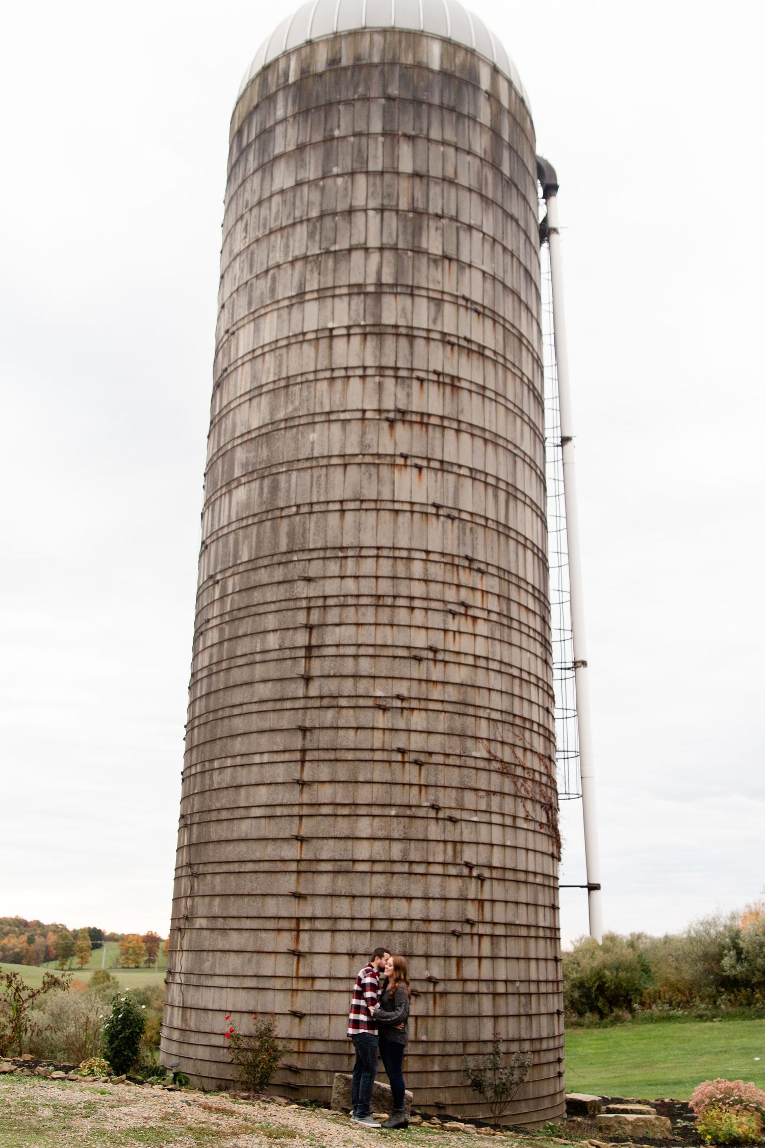 Large wooden grain silos stand tall against an overcast sky in a rural farm setting.