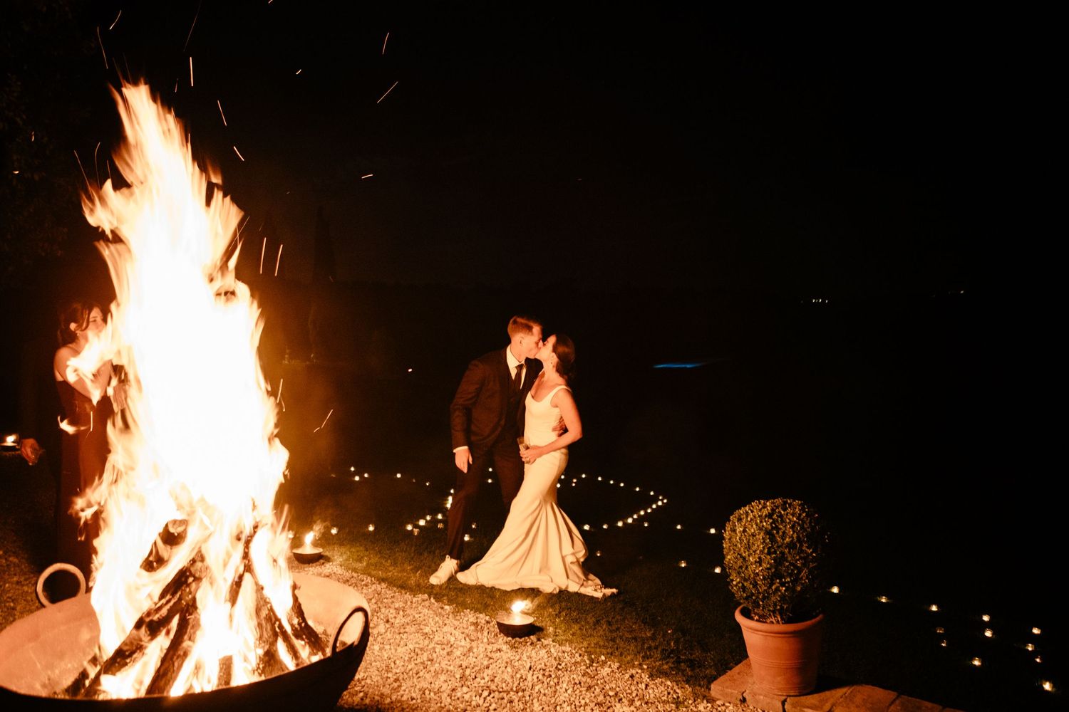 Bride and groom kiss by the bonfire at their evening reception of their wedding at The Lazy Olive in Tuscany.