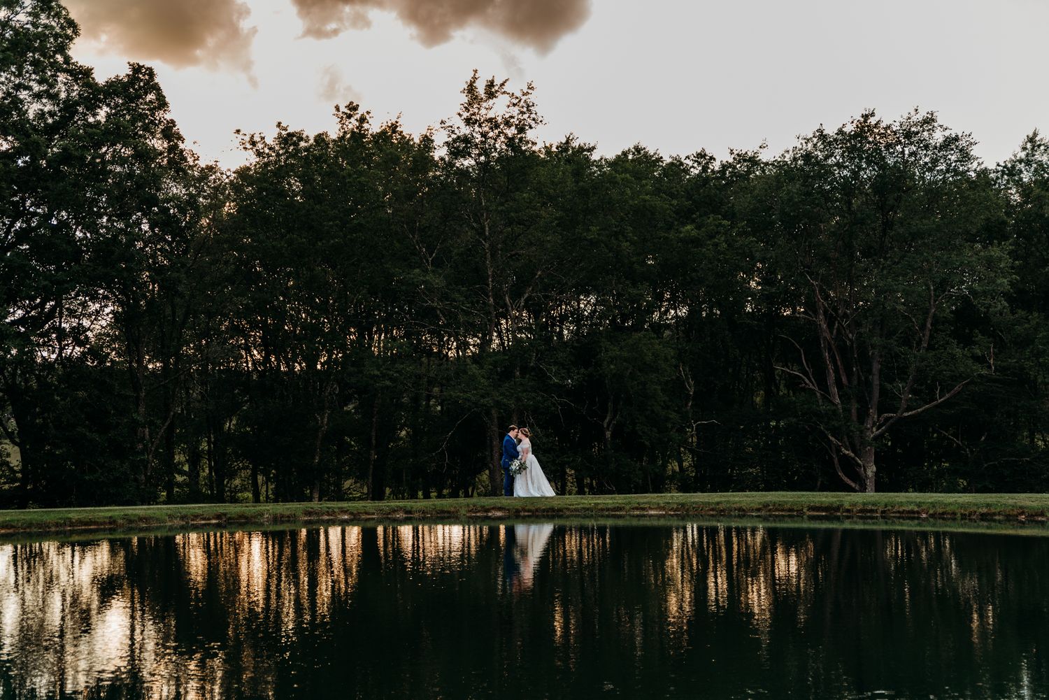 Bride and Groom embrace by a pond at during sunset at The White Barn at Lucas Farms in Oakland, MD