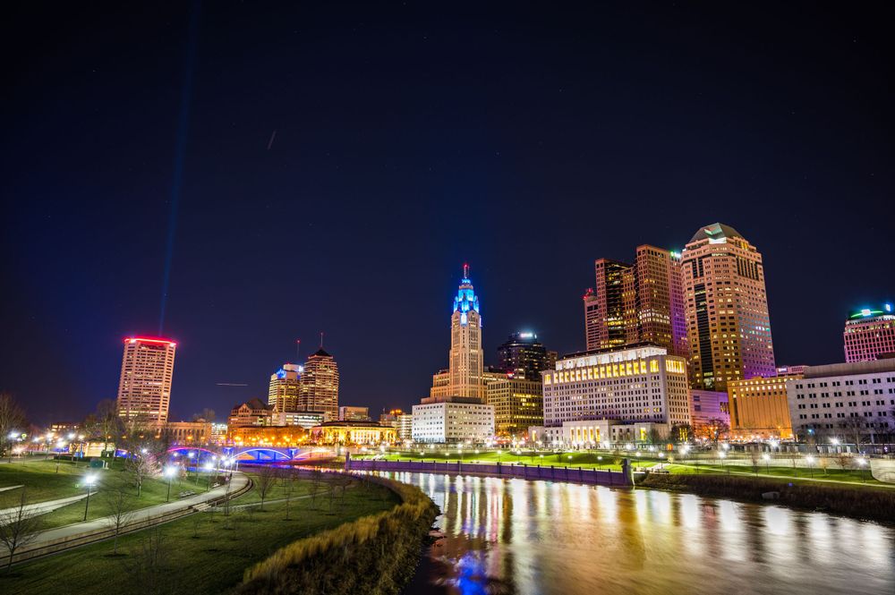 City skyline illuminated at night with colorful lights reflecting on the river.