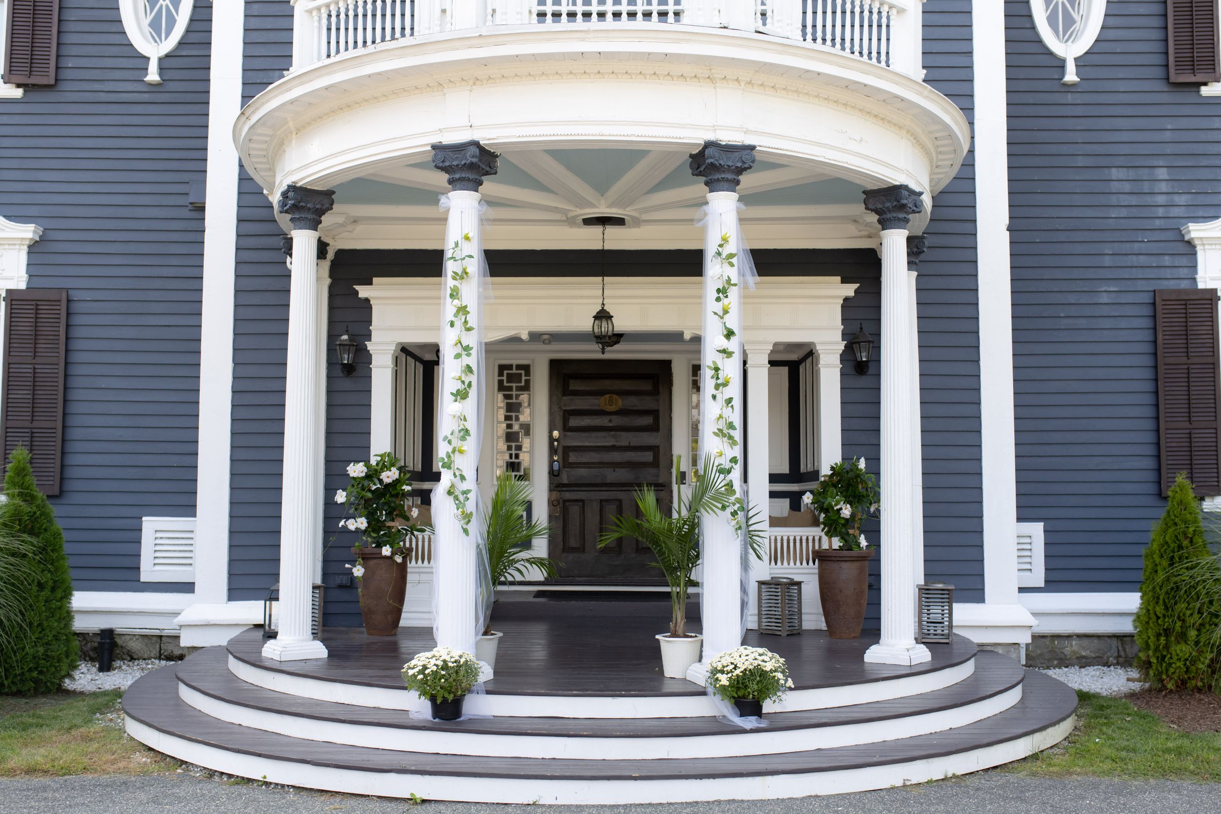 Elegant white columned entrance of a navy blue mansion with ornate architectural details and potted plants.