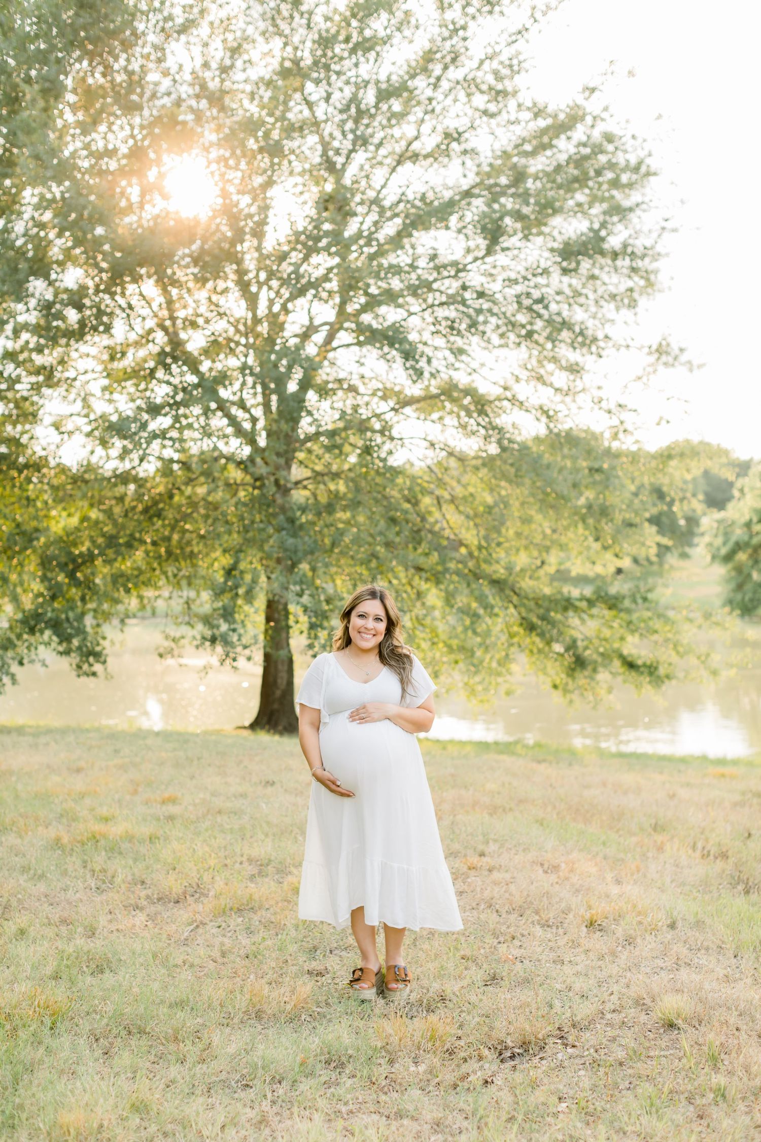 Woman in white dress stands in serene field setting during golden hour photography session.