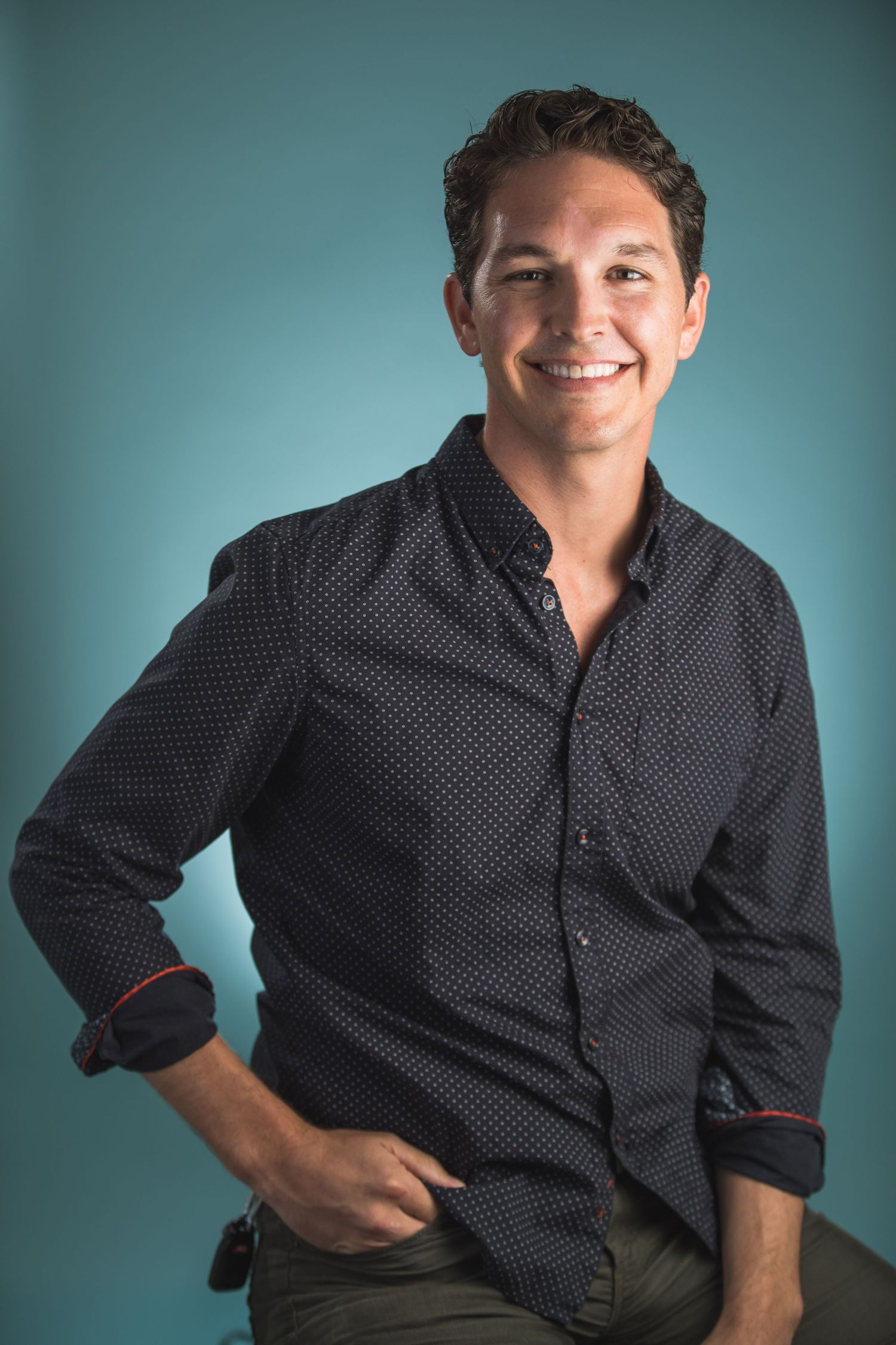Professional headshot against a teal backdrop featuring a polka dot button-down shirt.