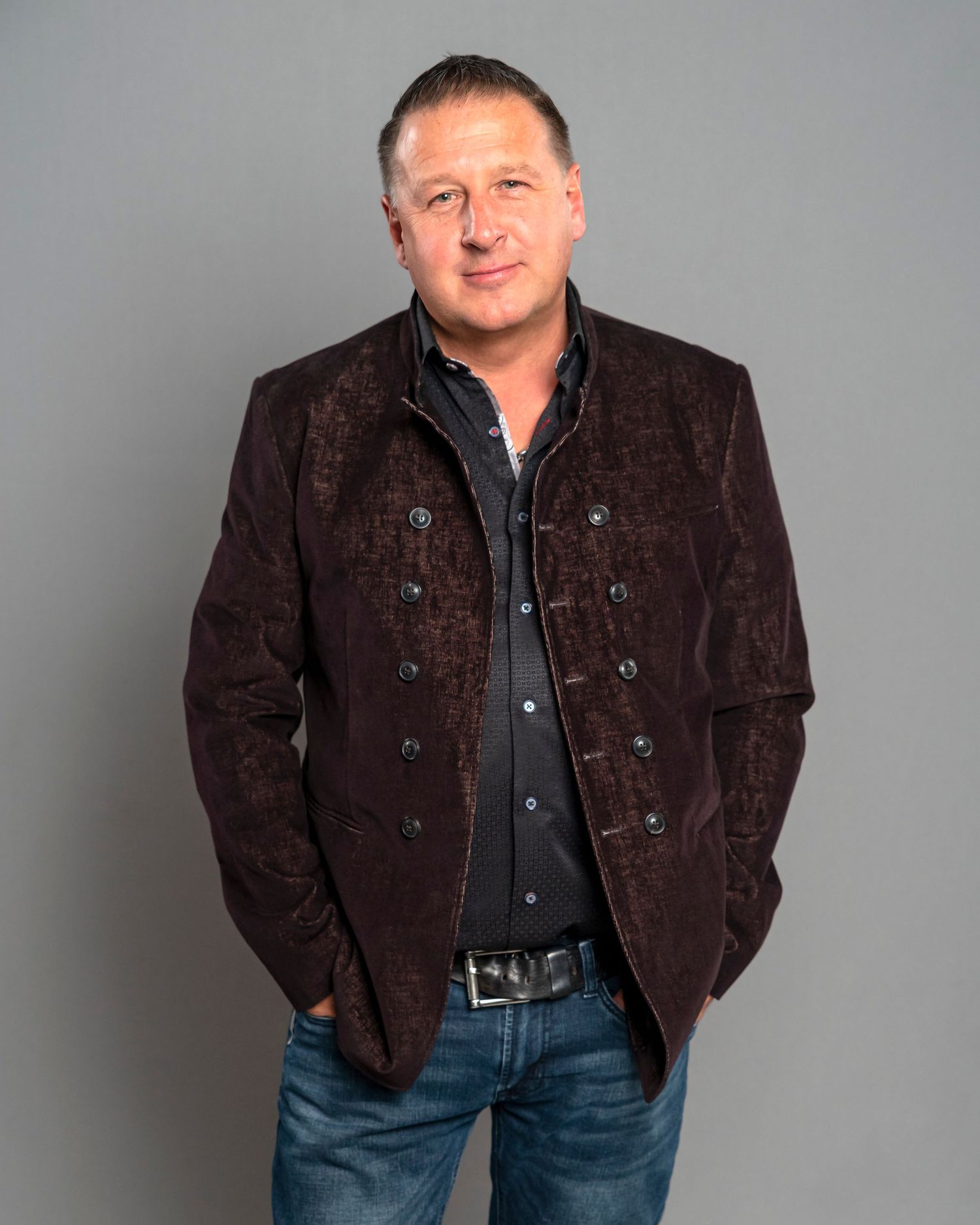 Portrait of man wearing brown textured jacket with buttons against grey background.