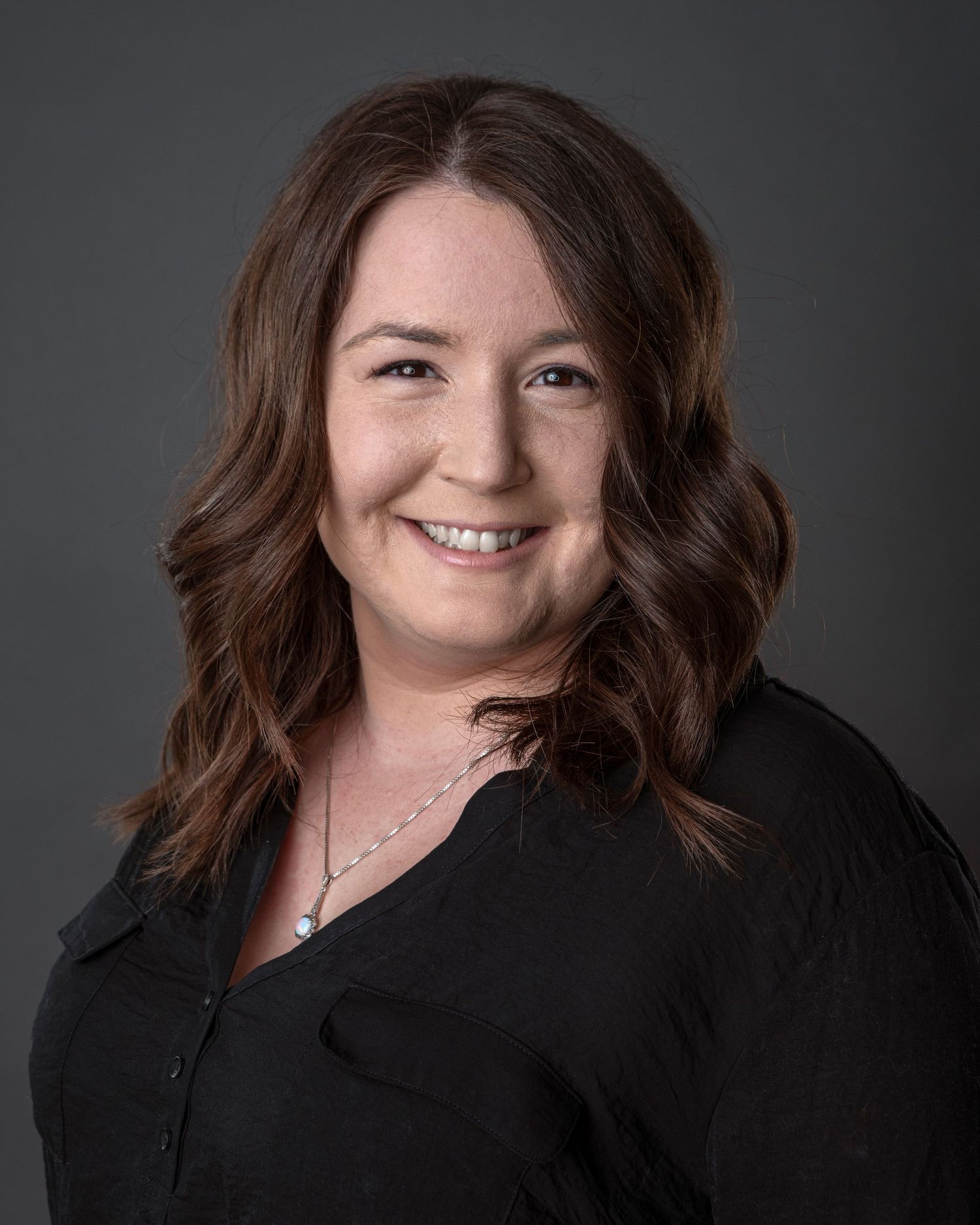 Professional headshot of woman in black top against dark background.