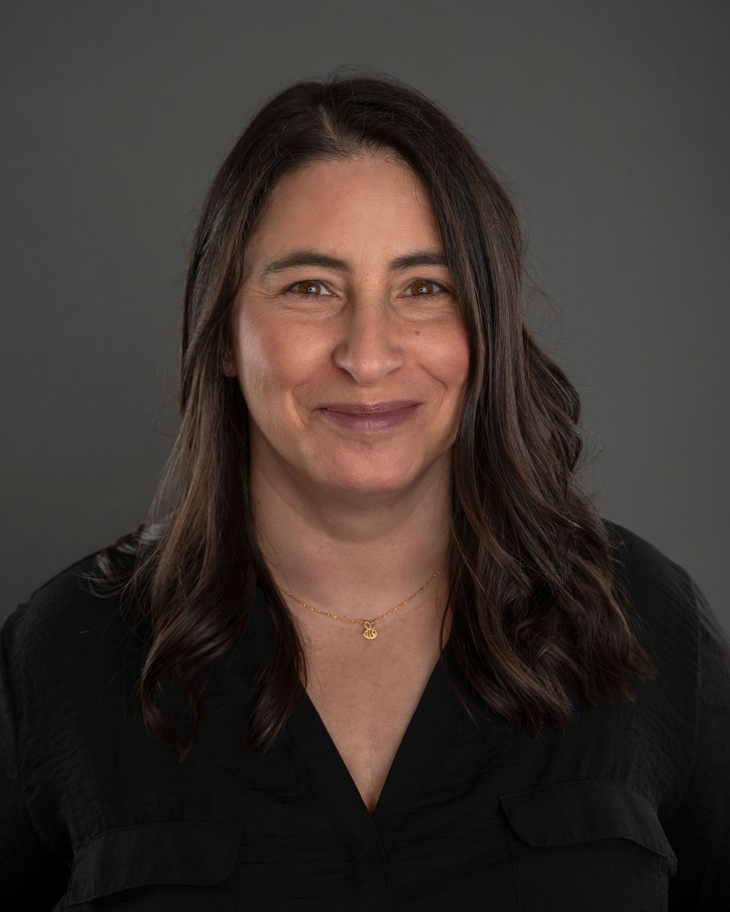 Professional portrait of woman in black top against dark grey background.