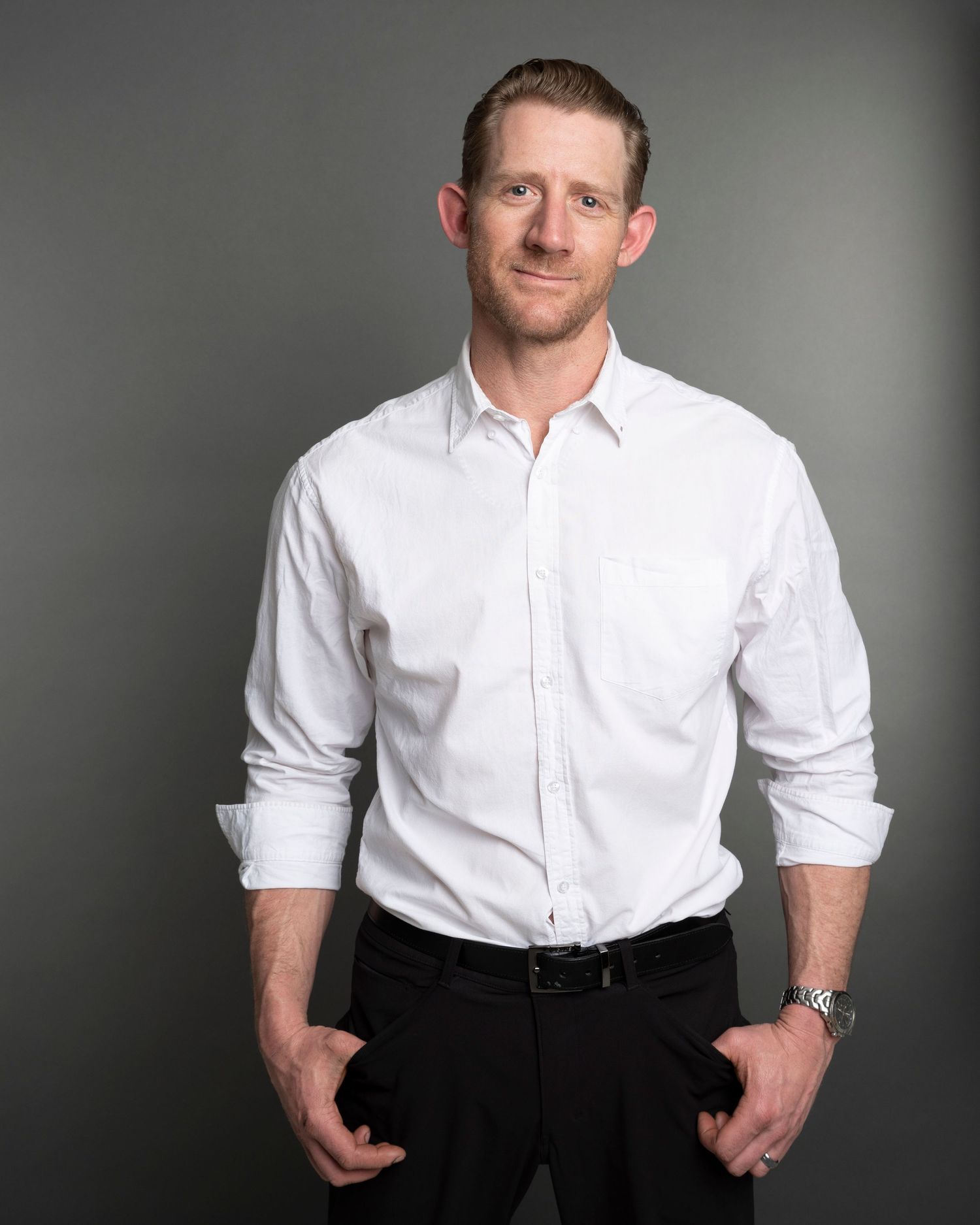 Professional portrait of person in white button-down shirt with rolled sleeves against grey backdrop.