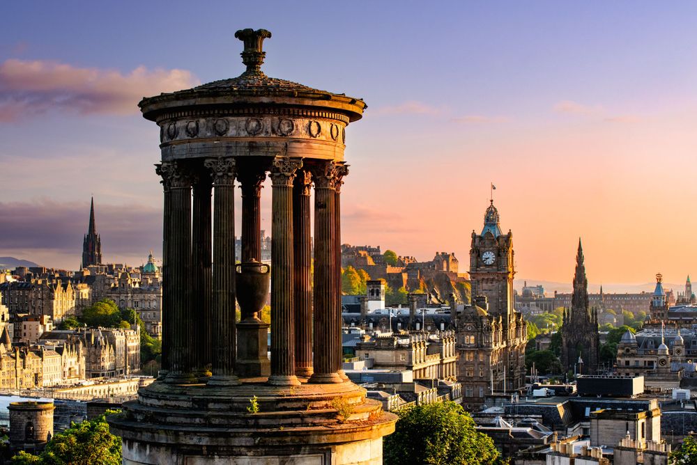 Dugald Stewart Monument silhouetted against Edinburgh's cityscape during a dramatic sunset.