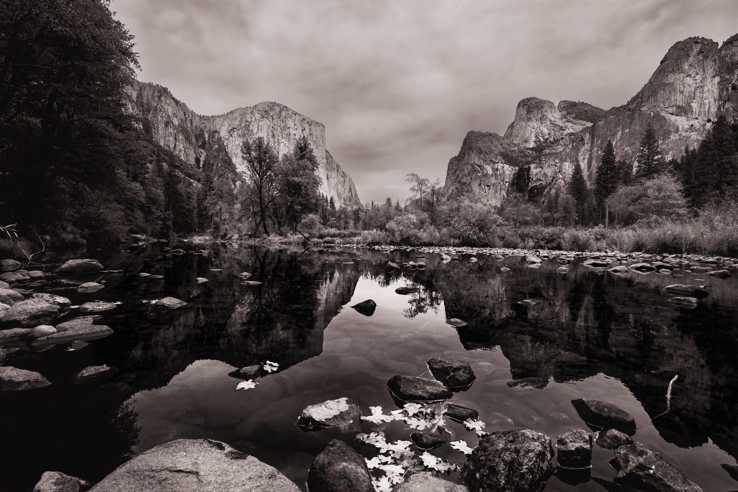 A black and white landscape of Yosemite Valley reflecting in calm waters with dramatic mountain peaks.