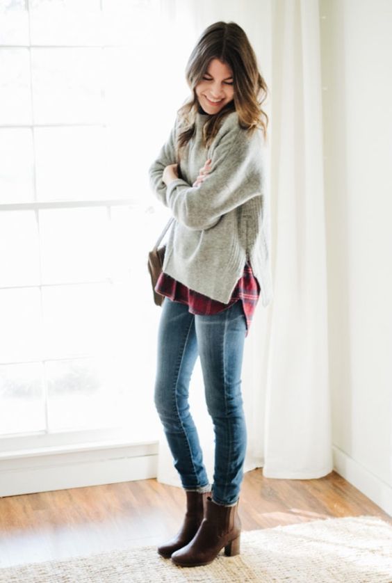 Layered winter look with oversized gray sweater over plaid shirt with skinny jeans and brown boots.