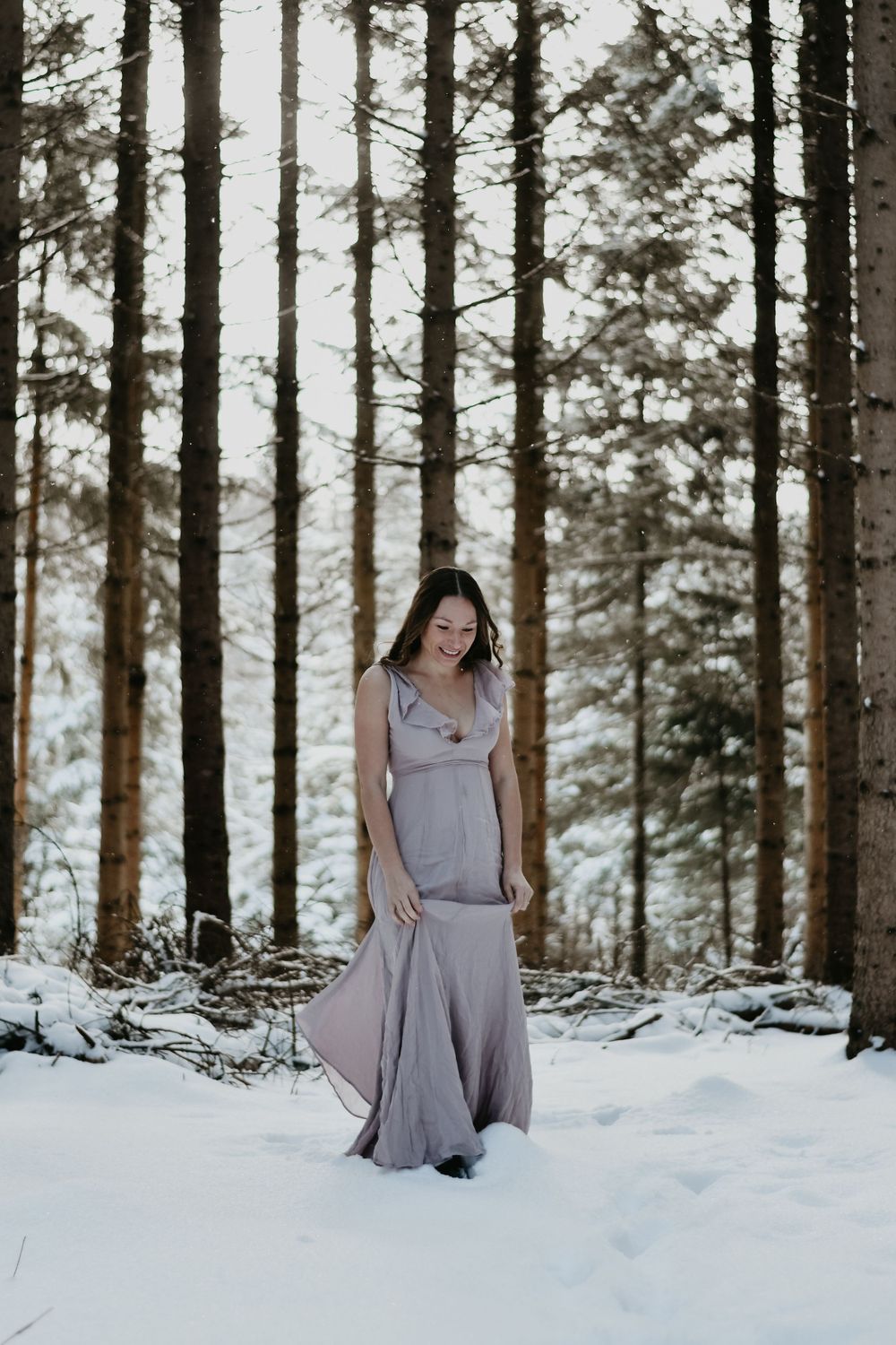 Full length portrait of person in flowing gray dress standing among snow-covered trees.
